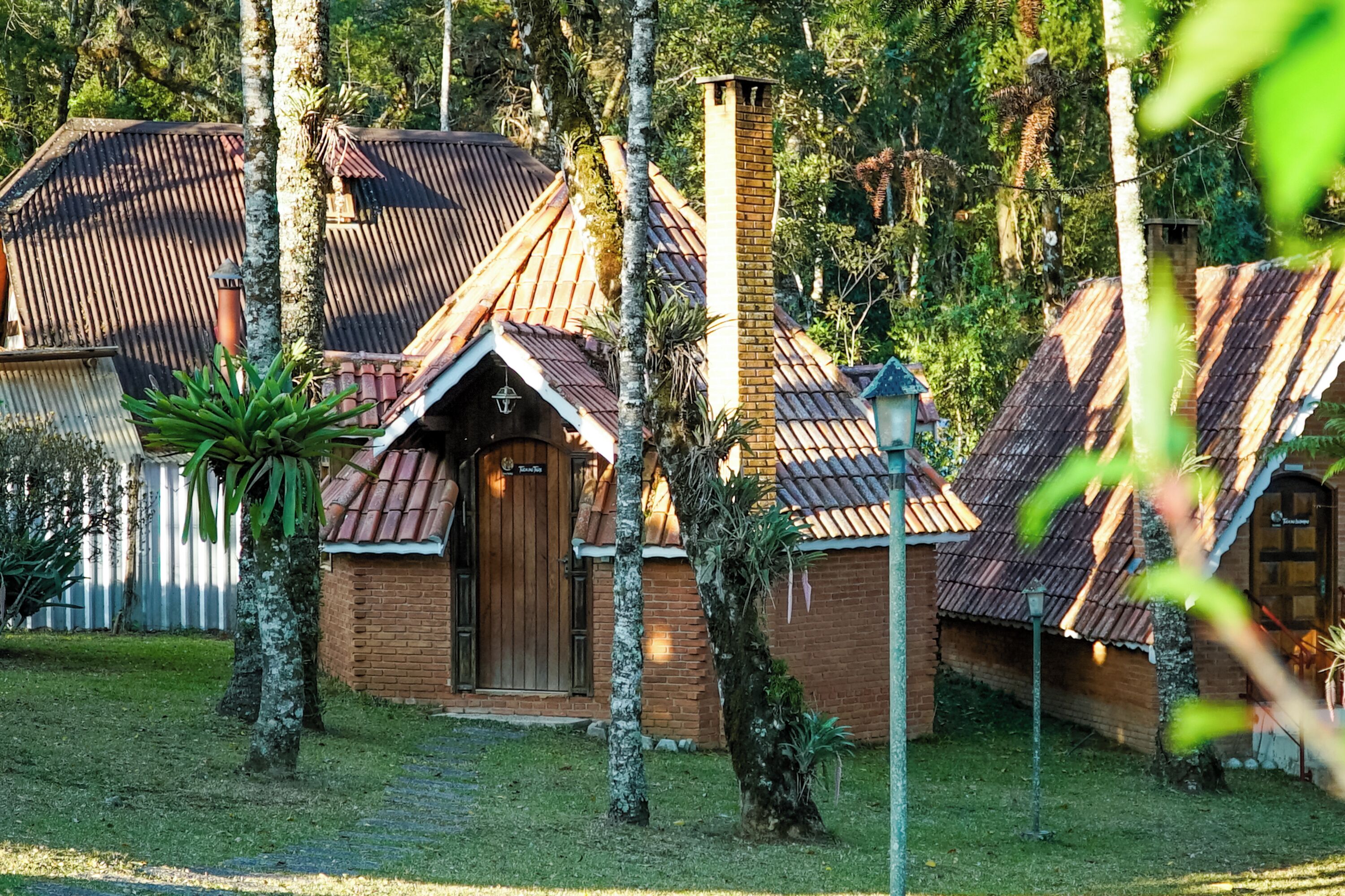 A rustic building with a brick exterior and a wooden door, surrounded by trees and a well-maintained lawn.