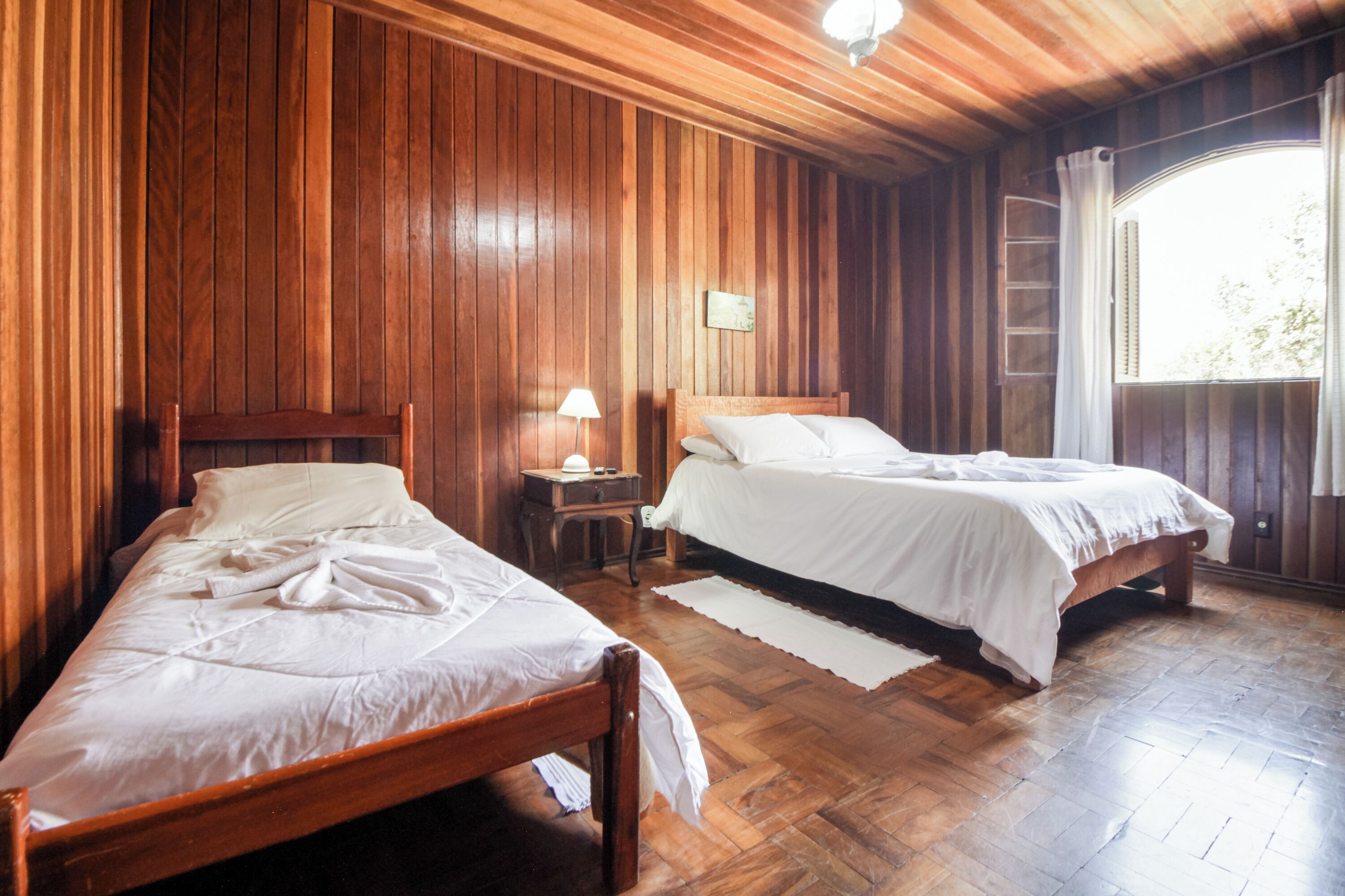 Una stanza con due letti in legno, un comodino con lampada e una finestra con tende.