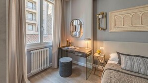 A bedroom with a bed, a desk with a lamp, a round ottoman, and a window with curtains. - Stunning Apartment with Ponte Vecchio and Arno River Views
 (Firenze)