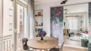 A modern living room with a round wooden table, black chairs, and a vase of purple flowers. There is a large window with a view of buildings outside. - Stunning Apartment with Ponte Vecchio and Arno River Views
 (Firenze)