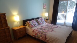 Un dormitorio con cama, mesitas de noche de madera, cómoda y ventana con vista a árboles.