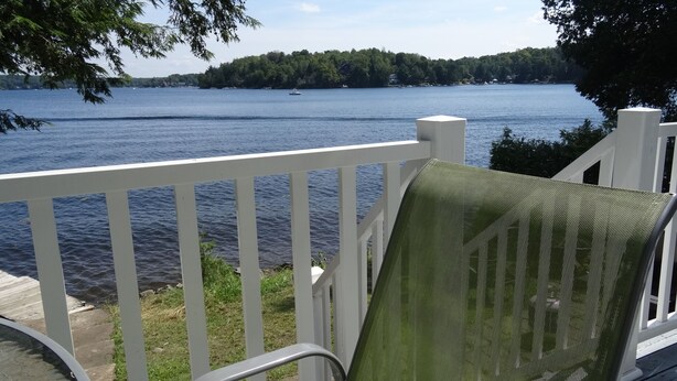 Una terraza con una silla verde, con vistas a un lago con barcos y una isla boscosa.