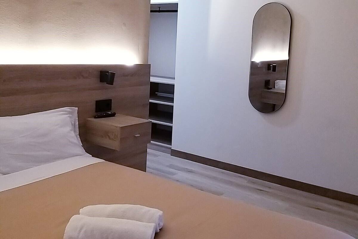 Une chambre d’hôtel moderne avec un lit bien fait, une table de chevet avec une télécommande et un miroir fixé au mur.