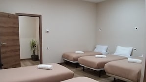 Een kamer met vier op een rij staande bedden, een houten deur, een potplant en inbouwspots.