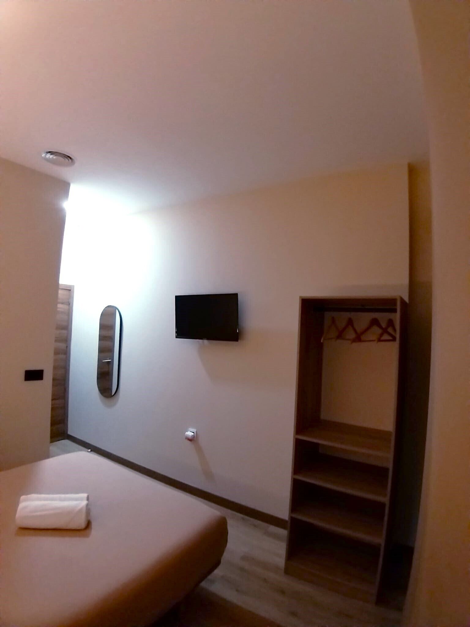 Habitación de hotel con cama, televisión montada en la pared, espejo y armario empotrado.