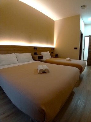 A hotel room with two beds, each with a headboard and bedside tables.