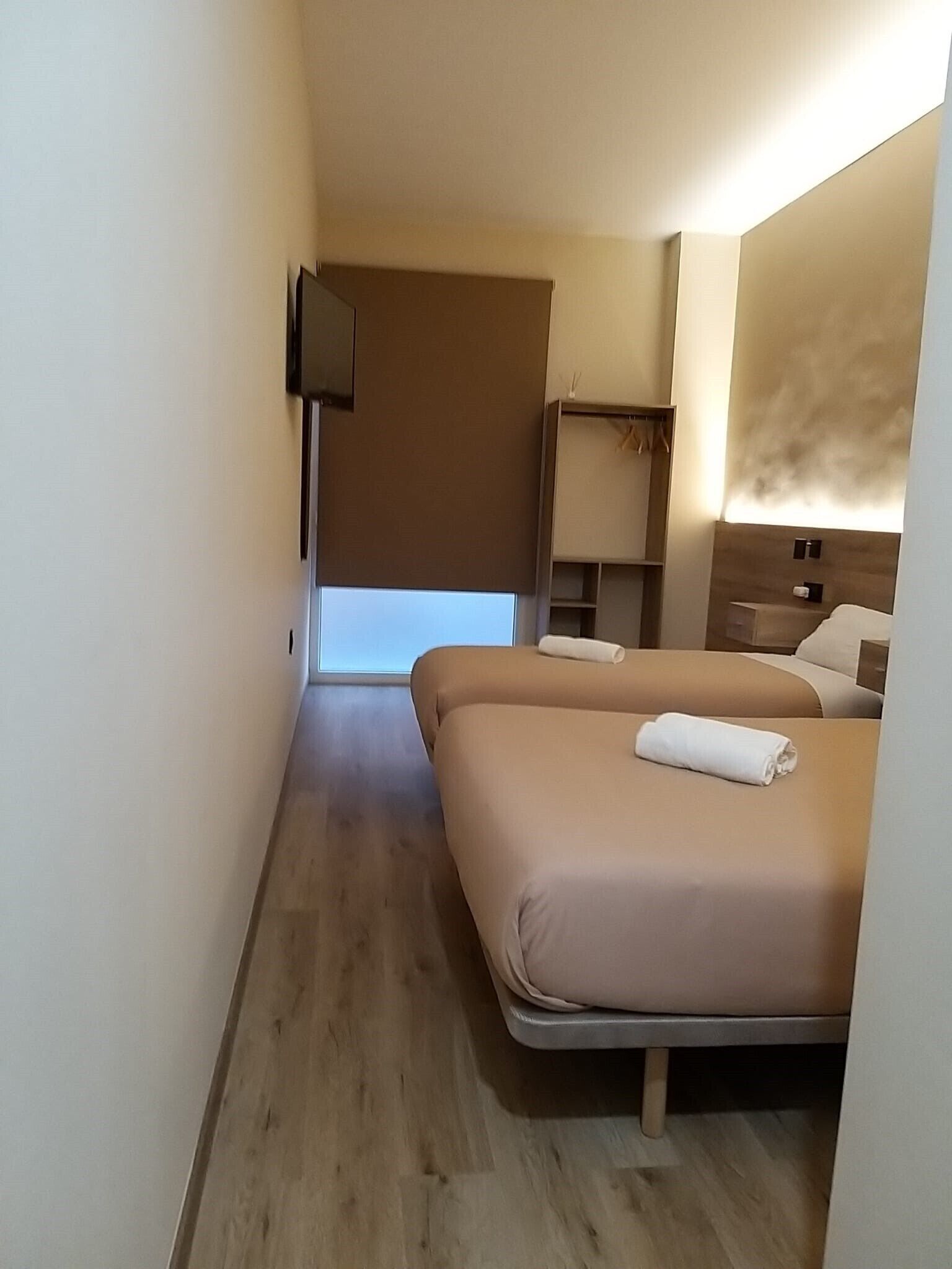 A hotel room with a bed, a TV mounted on the wall, a small desk, and a window.