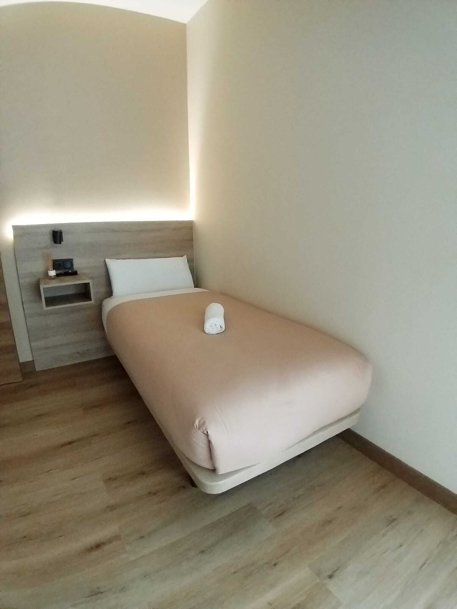 A minimalist hotel room with a single bed, a bedside table, and a nightstand.