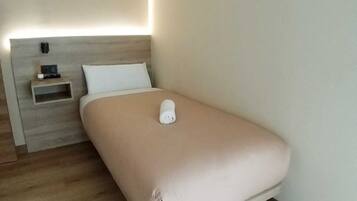 A minimalist hotel room with a single bed, a bedside table, and a nightstand.