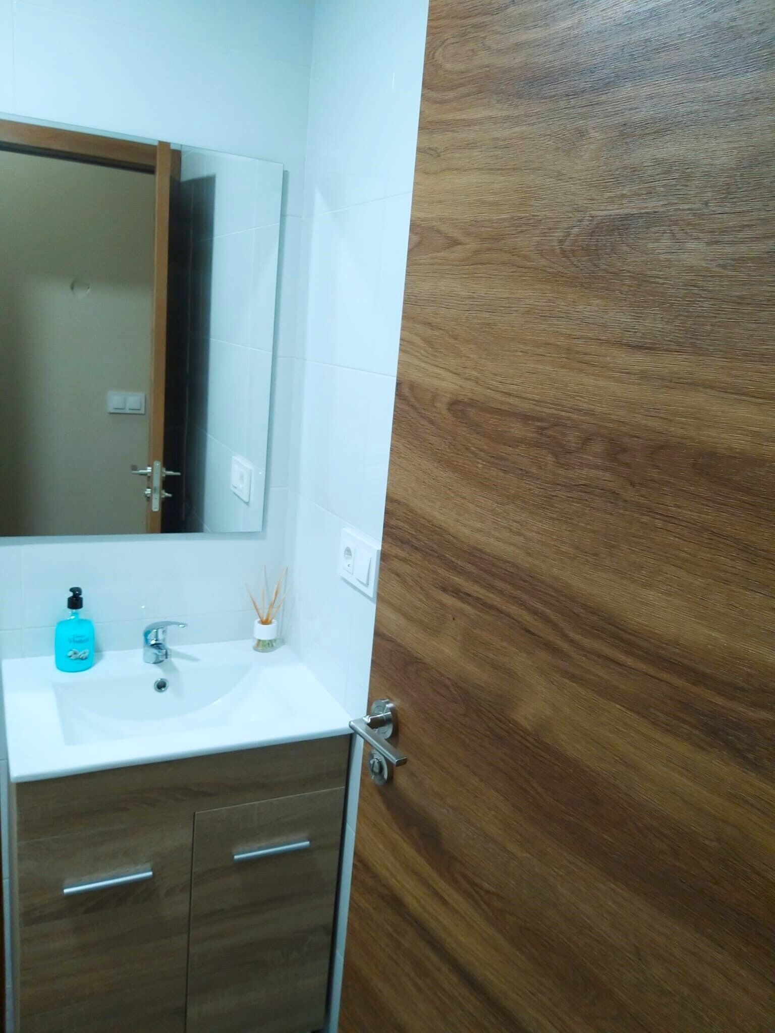 Un baño con un lavamanos blanco, un espejo y armarios de madera.
