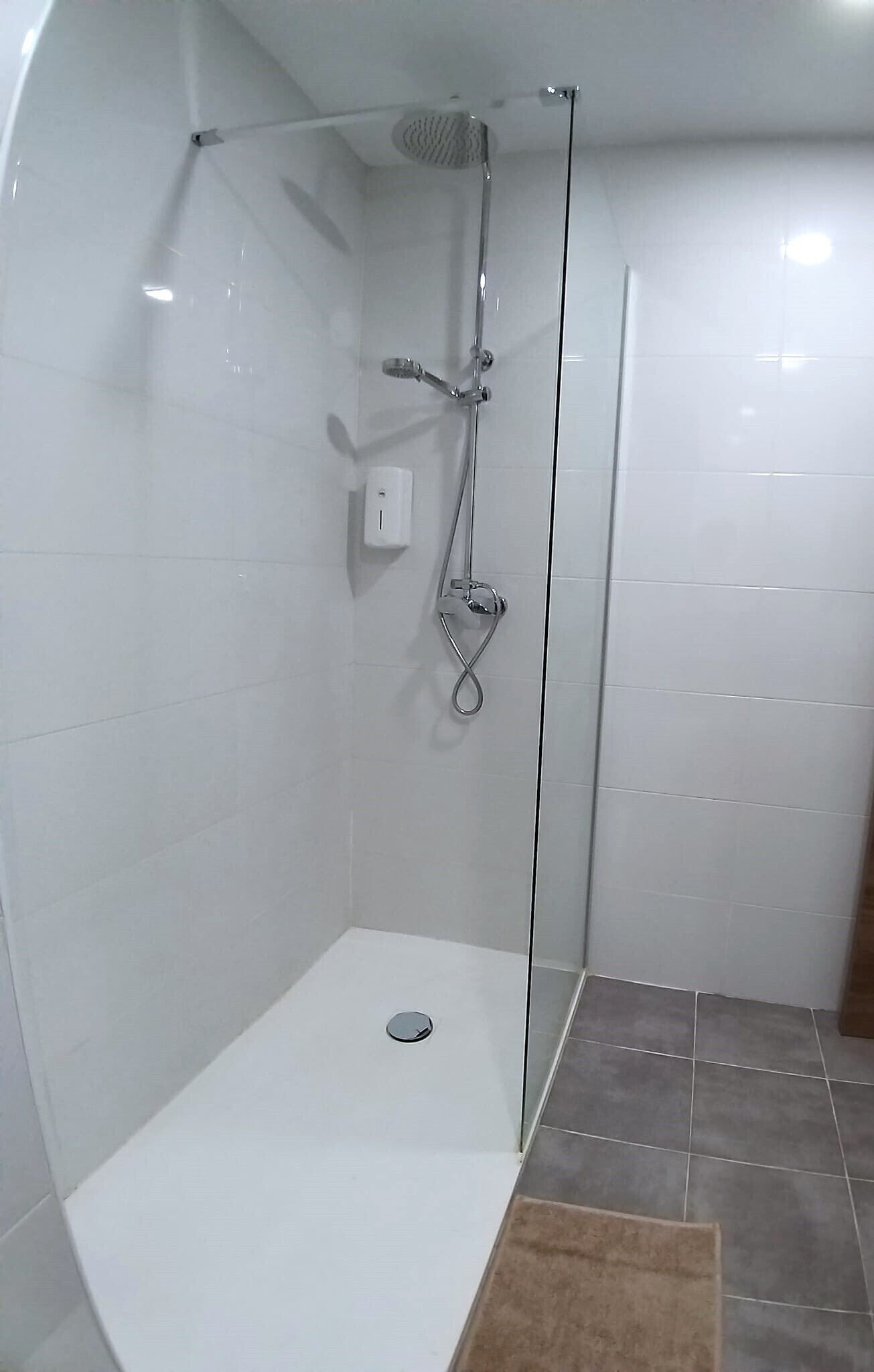 Una ducha moderna con puerta de vidrio, un cabezal de ducha de mano y un grifo empotrado.