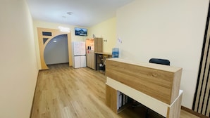 Een kleine kantoorruimte met kitchenette, een grote waterkoeler en een flatscreen televisie aan de muur.