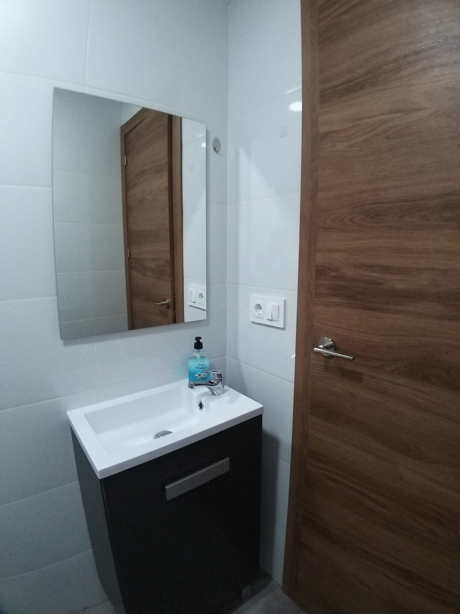 Un baño con un lavabo blanco, un espejo y una puerta de madera.