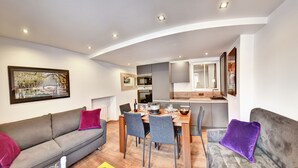 A modern living room with a grey sofa, a dining table with chairs, and a kitchen area with a built-in oven and microwave. - Cozy apartment between lake and mountains (Annecy)