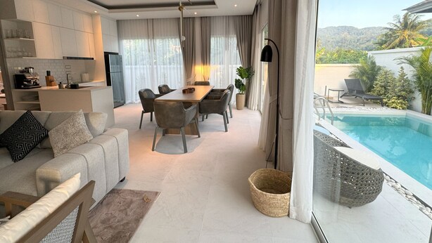 A modern living room with a dining area, a kitchen, and a view of a swimming pool. - Deluxe Kamala pool villa with maid (Kamala)