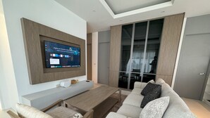 A modern living room with a flat-screen TV mounted on the wall, a sofa, a coffee table, and a chair. - Deluxe Kamala pool villa with maid (Kamala)