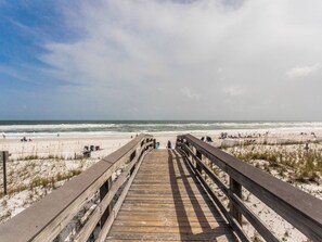 Une promenade en bois menant à une plage où se trouvent des personnes et des chaises de plage.