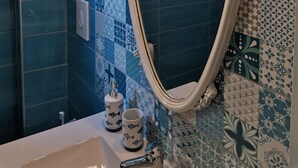 A bathroom with a blue tiled wall, a white sink, and a decorative mirror.