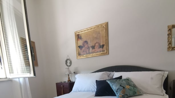 A neatly made bed with a blue bedspread and white towels, a nightstand with a lamp, a framed picture on the wall, and a window with blinds.