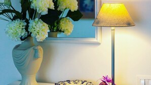 A white vase with flowers on a table, a mirror, and a lamp.