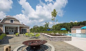 Zona de piscina con mobiliario exterior, una chimenea y un edificio con garaje.