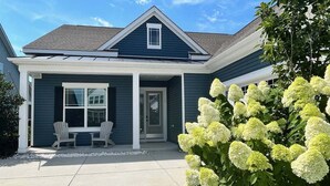 Een huis met twee verdiepingen, een veranda, een overdekte ingang en een kleine tuin met witte bloemen.