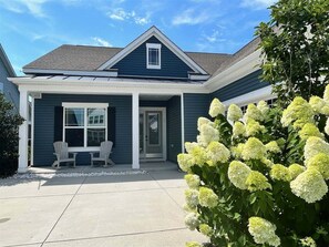 Ein zweigeschossiges Haus mit einer Veranda, einem überdachten Eingangsbereich und einem kleinen Garten mit weißen Blumen.