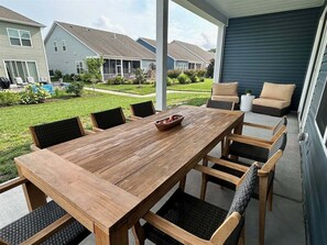 Eine überdachte Terrasse mit einem Holztisch und Stühlen, ein kleiner Garten und Blick auf Nachbarhäuser.