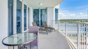Ein Balkon mit Glastisch und zwei Stühlen, mit Blick auf ein Schwimmbad und Grünflächen.