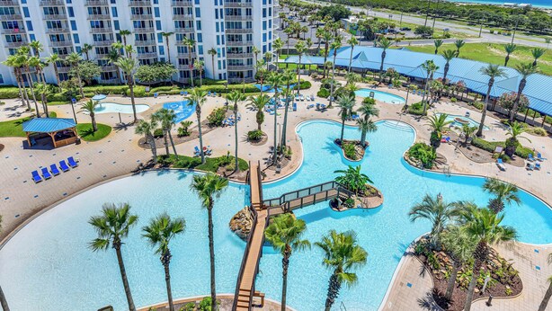 Ein Resort mit mehreren Schwimmbecken, Palmen und einem großen Gebäude im Hintergrund.