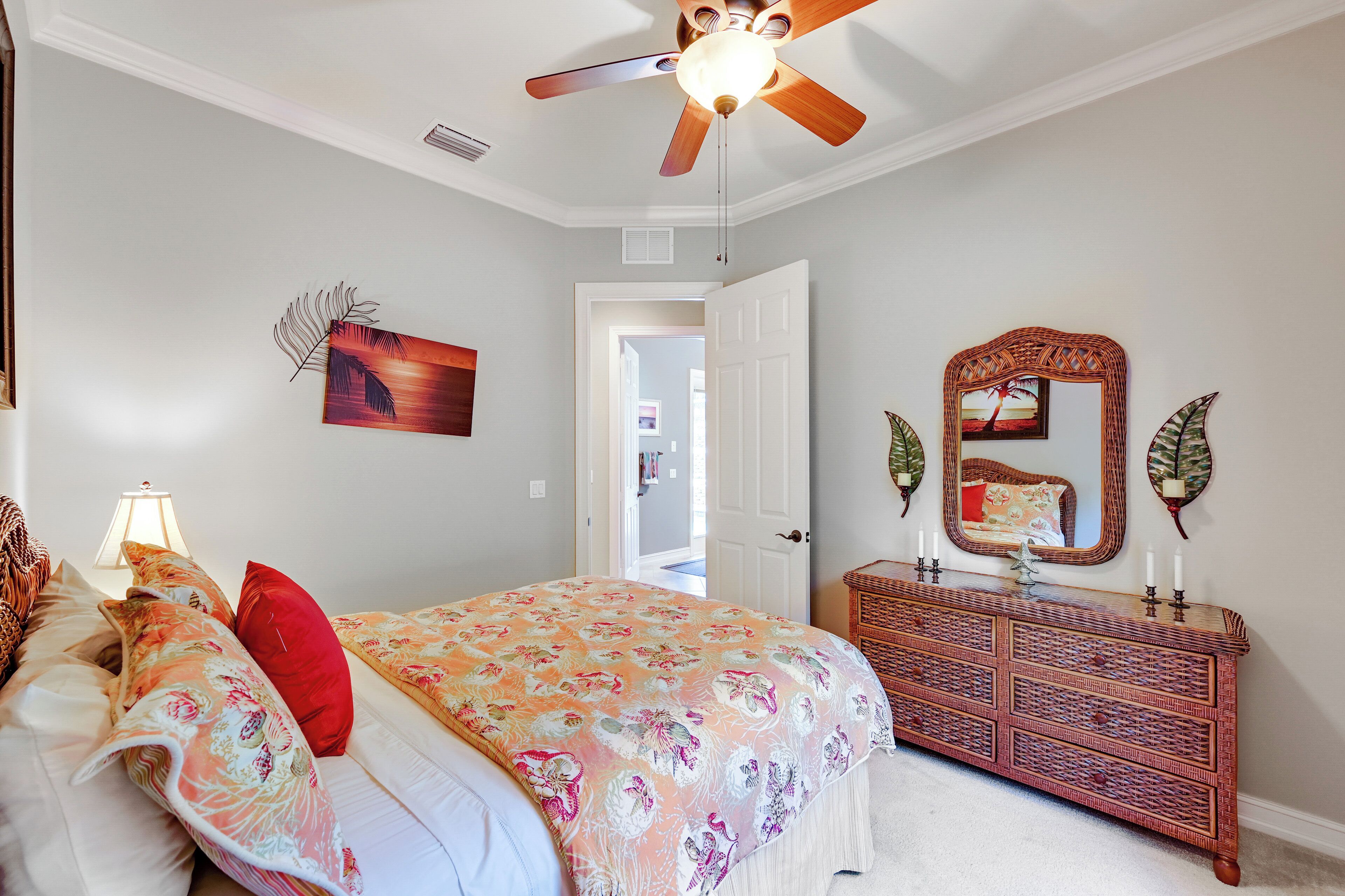 A bedroom with a bed, a dresser, a ceiling fan, a door, and wall decorations.