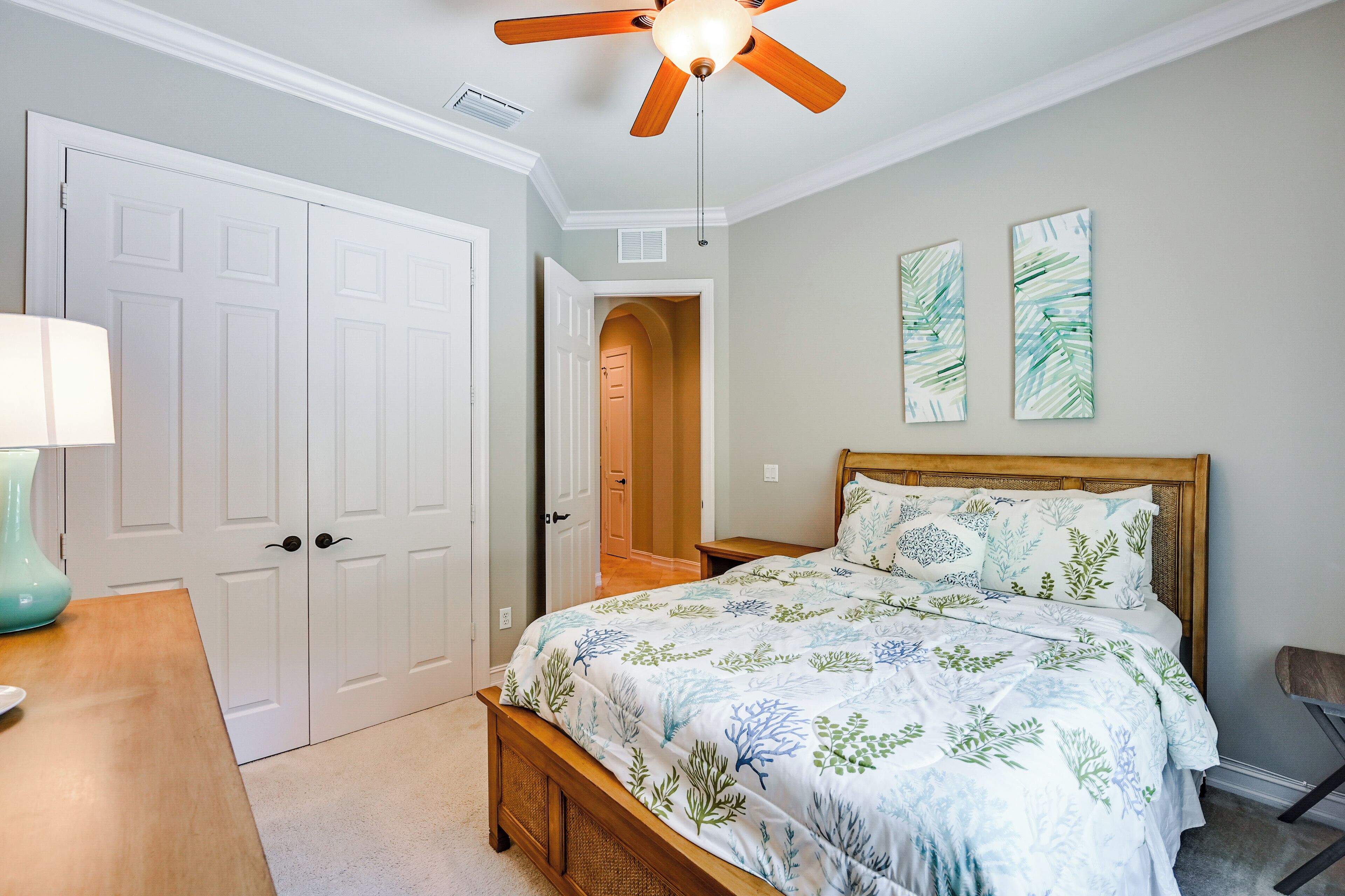 Ein Schlafzimmer mit Bett, Deckenventilator, Nachttisch, Lampe und Tür.