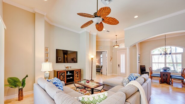 A spacious living room with a large ceiling fan, a sofa set, a dining area with chairs, and a kitchen in the background. - Marco Island Home w/ Private Pool: 3 Mi Beach! (Marco Island)