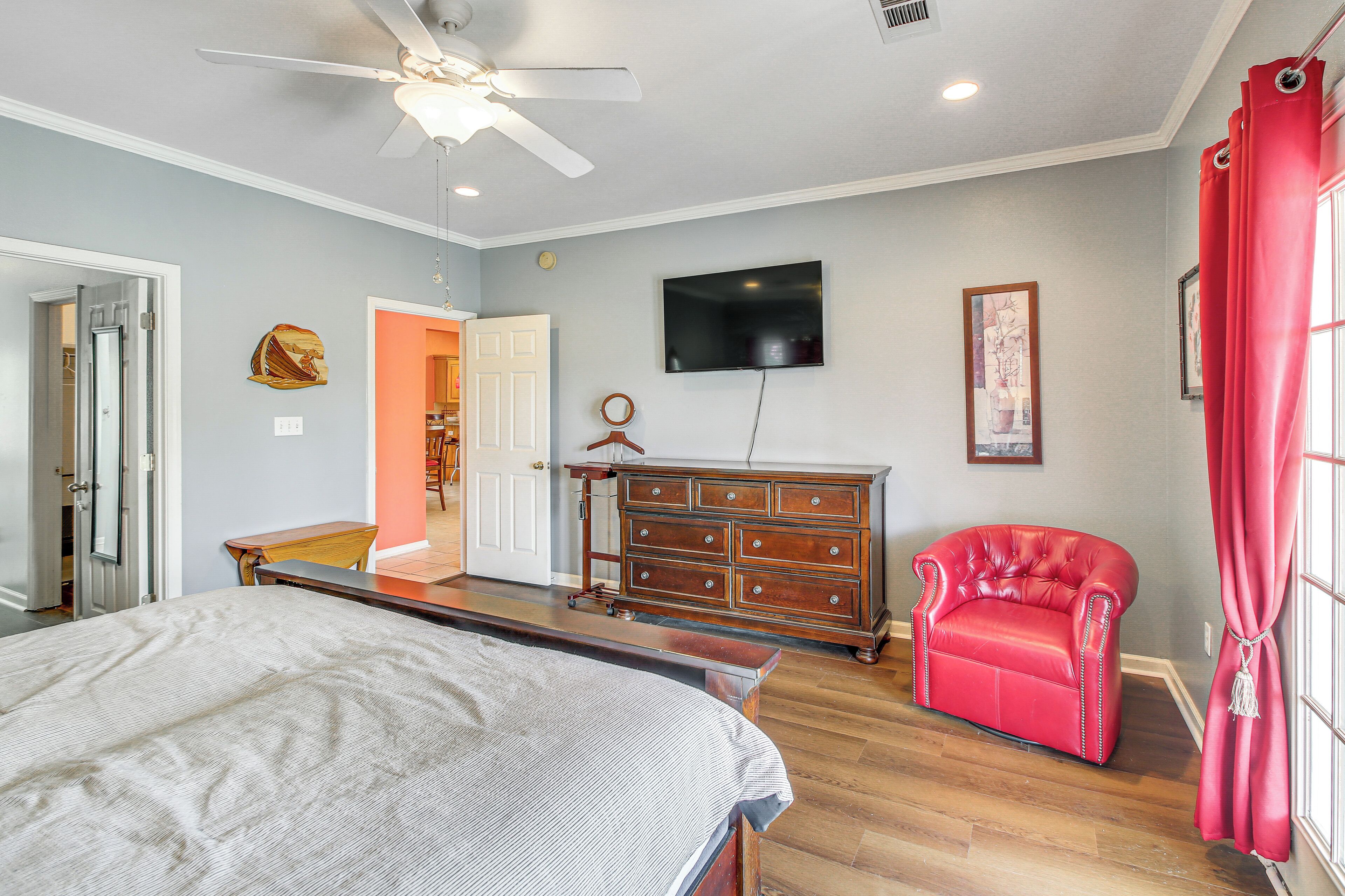 Un dormitorio con cama, cómoda, televisor y una silla roja.