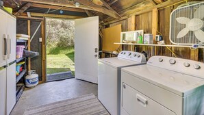 Un área de lavandería con lavadora y secadora, un ventilador y un estante con productos de limpieza.