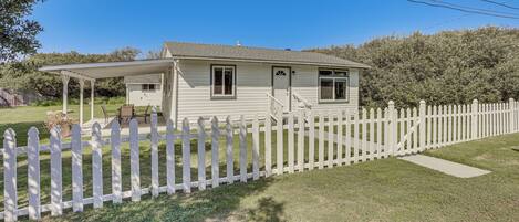 A single-story house with a white picket fence, a covered porch, and a small front yard.