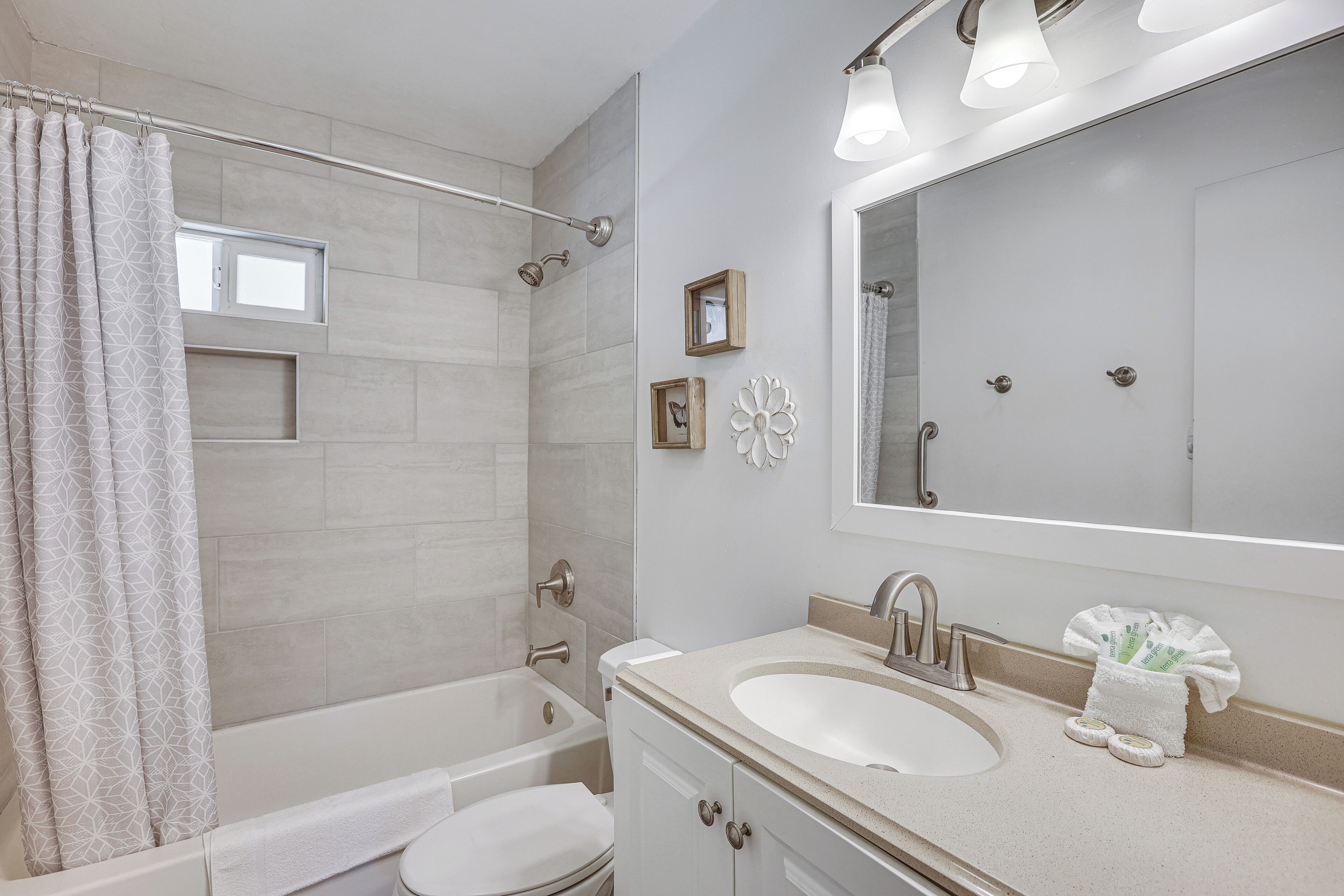A bathroom with a bathtub, toilet, sink, and a large mirror.