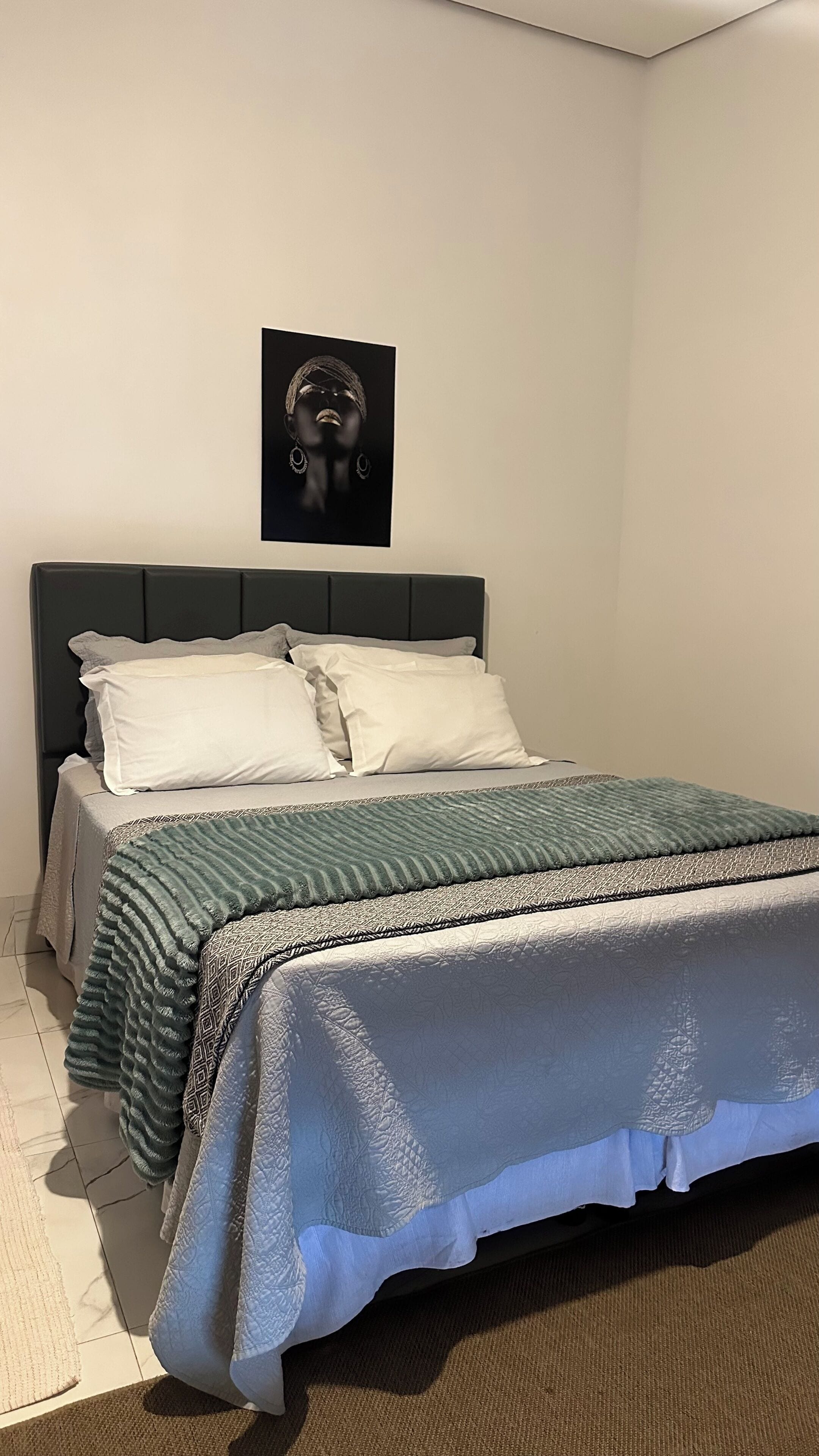 Un dormitorio con cama, almohadas, cabecera y un cuadro colgado en la pared.