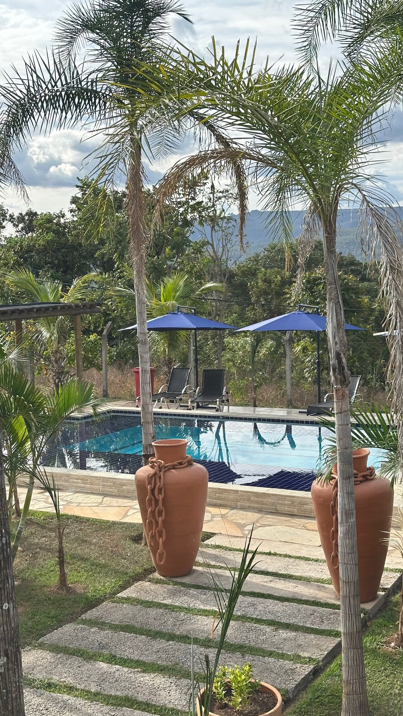 A pool area with two terracotta planters, a seating area with chairs and umbrellas, and a view of the surrounding landscape.
