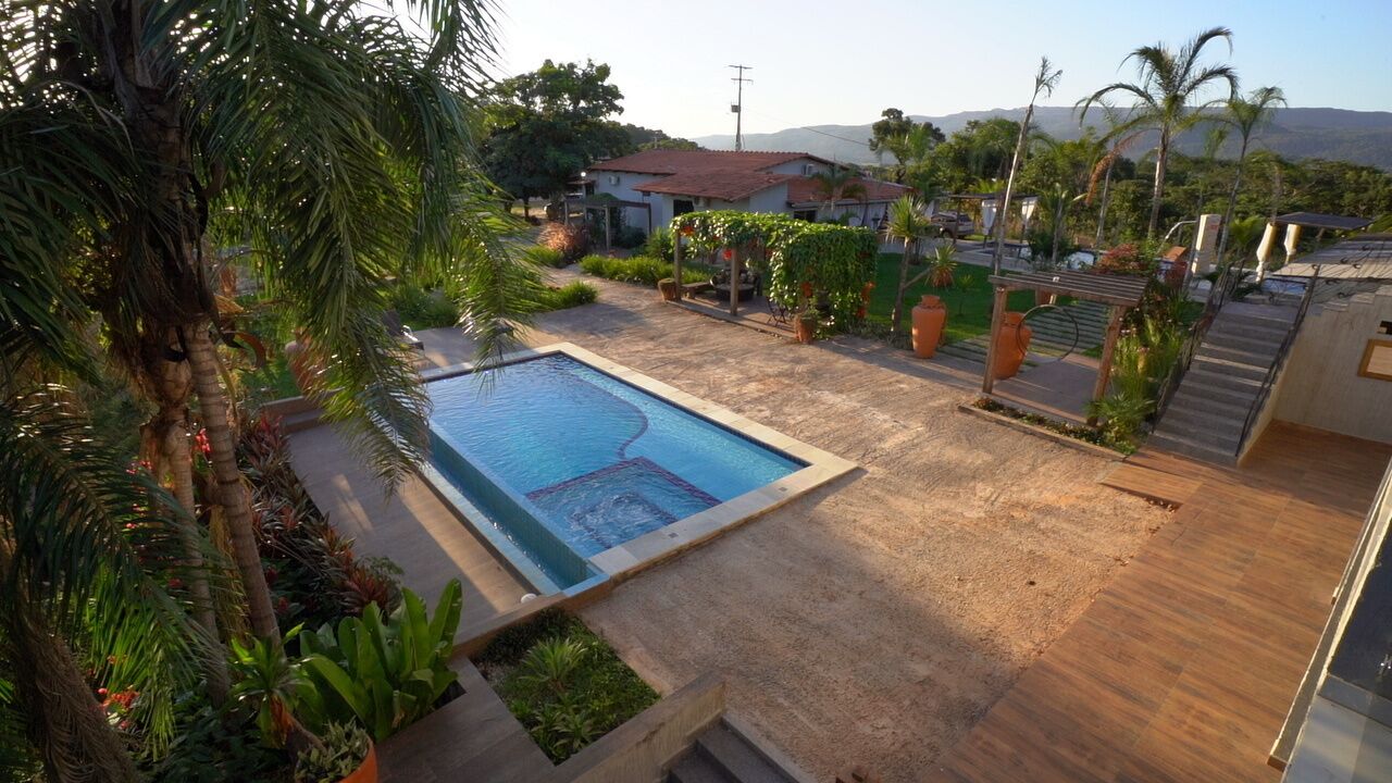 Una piscina rodeada de plantas y una terraza de madera, con casas y montañas al fondo.