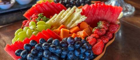 A fruit platter with various fruits and a decorative vase in the background.