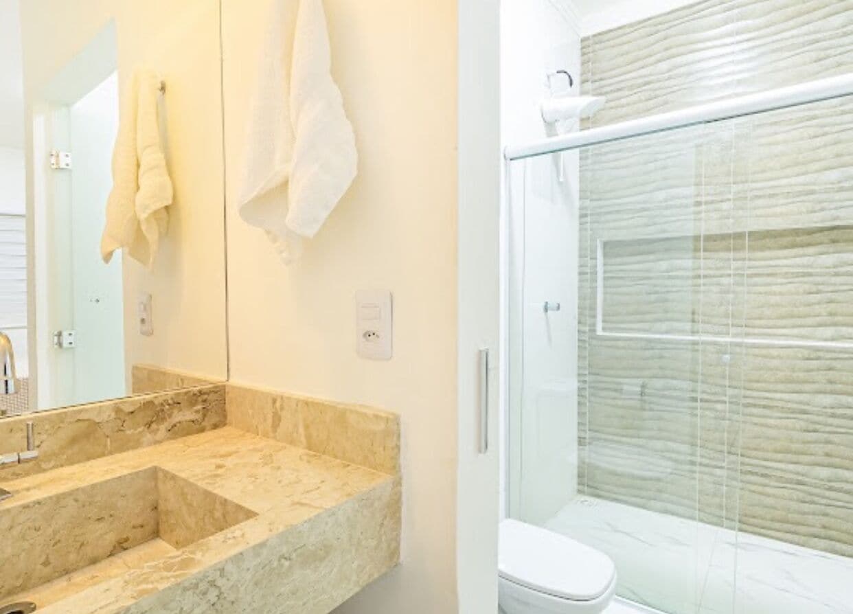 A bathroom with a marble sink, a mirror, and a glass shower enclosure.