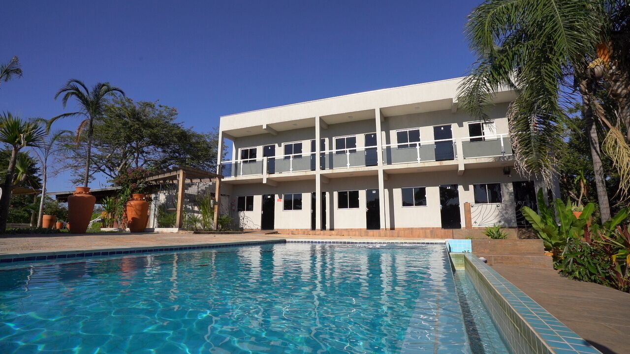 Un hotel de varios pisos con piscina, rodeado de palmeras y plantas en macetas.