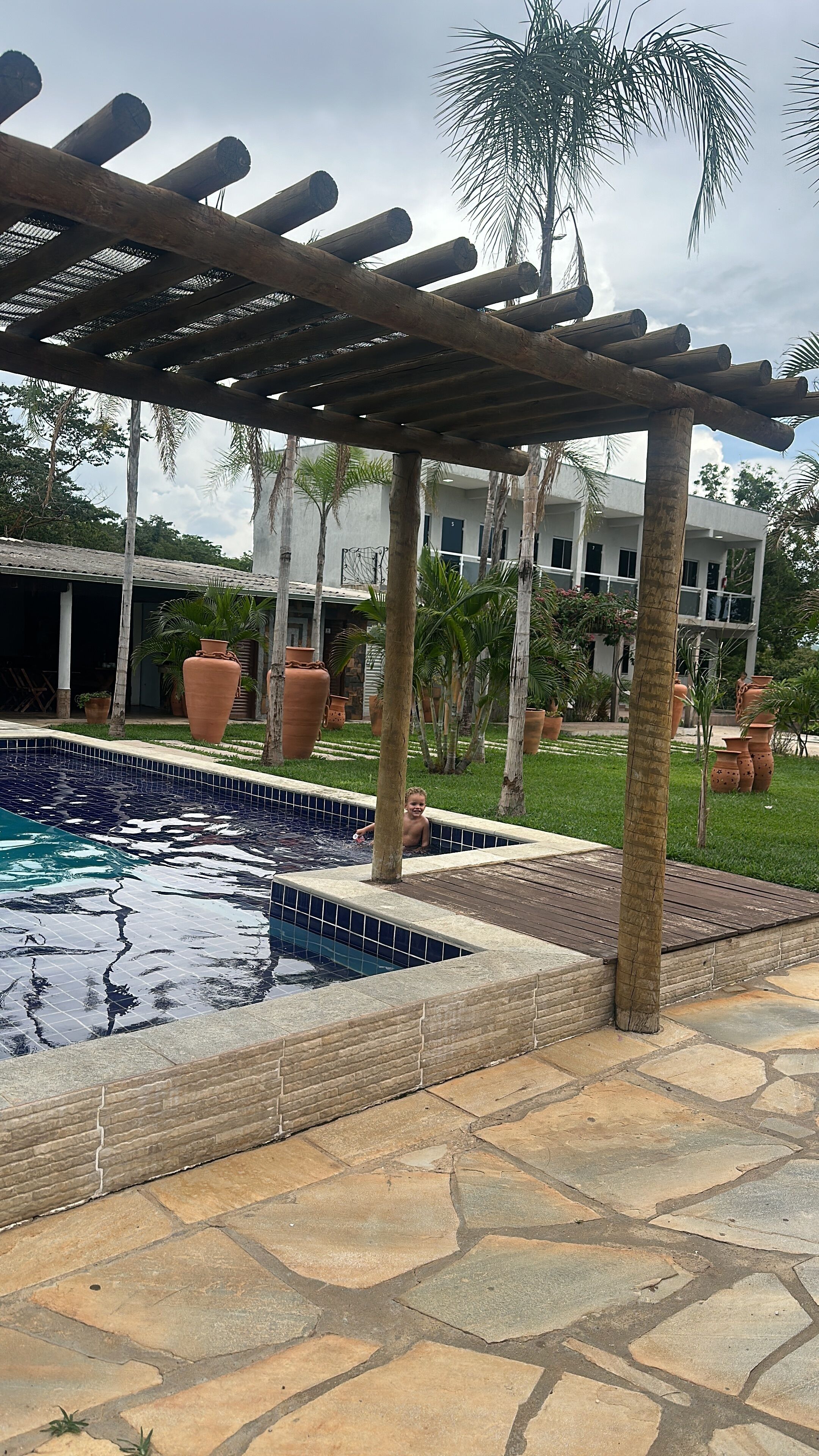 A pool area with a pergola, stone tiles, and large terracotta pots.