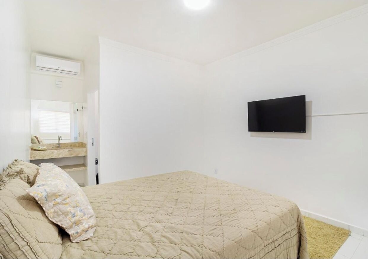 A bedroom with a bed, a television mounted on the wall, and a bathroom with a sink and mirror.