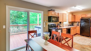 A kitchen with wooden cabinets, a black refrigerator, and a dining area with a table and chairs. - Campton Cottage w/ Hot Tub, Near Hiking + Climbing (Campton)