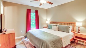 A bedroom with a bed, nightstands, a ceiling fan, a window with red curtains, and a wooden dresser. - Campton Cottage w/ Hot Tub, Near Hiking + Climbing (Campton)