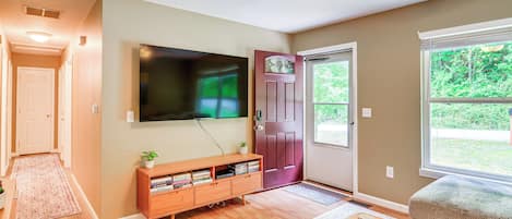 Una sala de estar con televisor de pantalla plana, mueble de madera para entretenimiento y ventana con vistas a follaje.