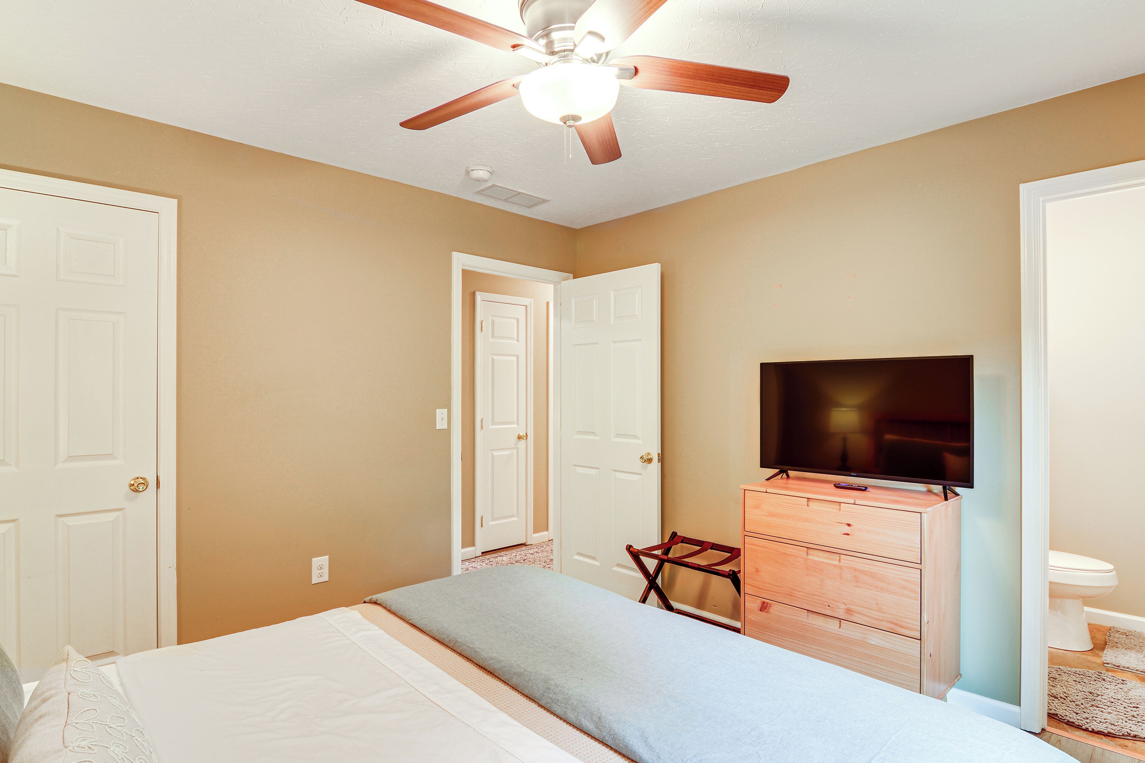 A bedroom with a bed, a dresser, a television, and a ceiling fan.