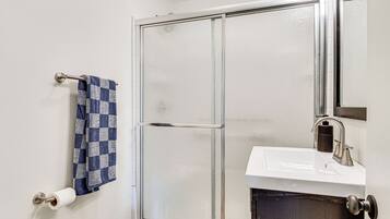 Un baño con cabina de ducha, lavamanos, toallero con una toalla a cuadros y dispensador de papel higiénico.